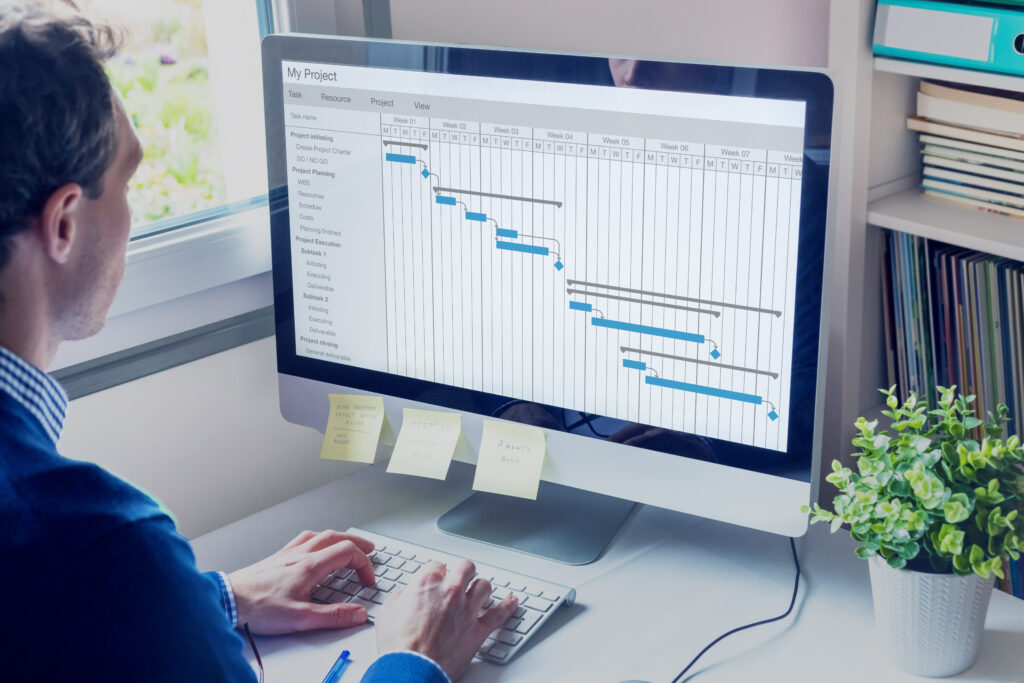 Project manager working on Gantt chart schedule to create planning with tasks and milestones to plan activities, person working with management tools on computer in office