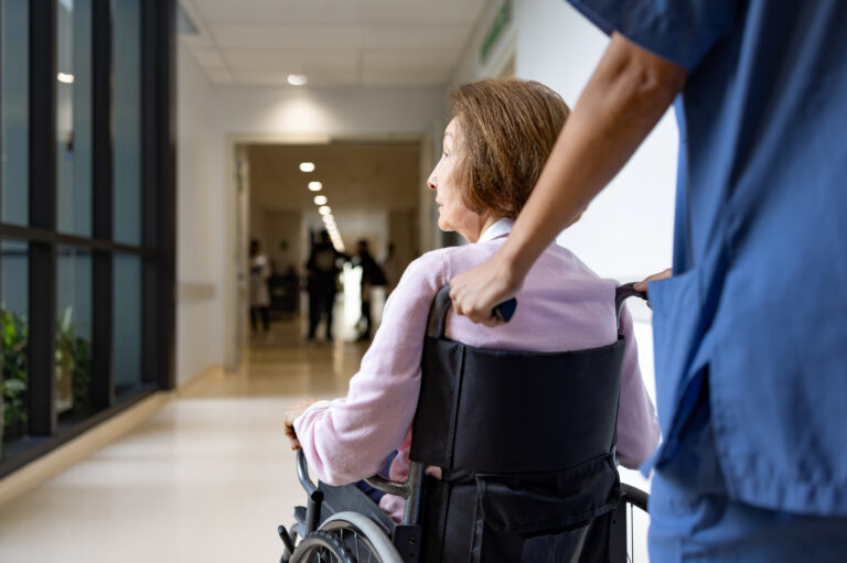 Rear view of a nurse pushing a senior woman in a wheelchair at the hospital